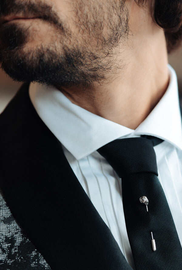 A man dressed formally with a black tie and a silver skull stud tie pin.
